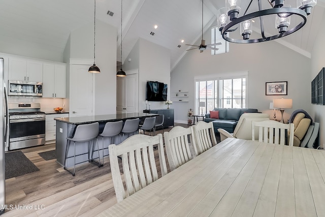 dining room featuring beam ceiling, high vaulted ceiling, ceiling fan with notable chandelier, and light hardwood / wood-style floors