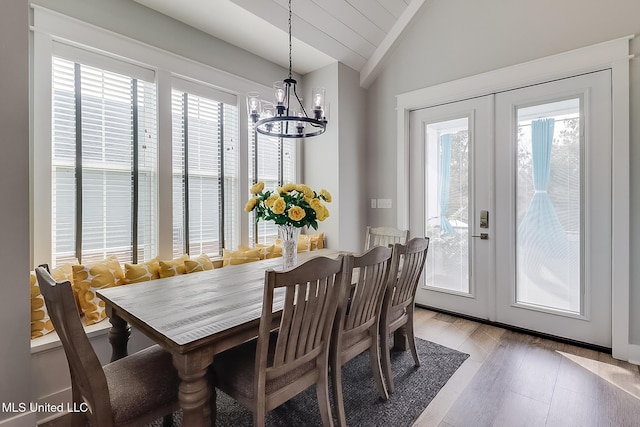 dining area featuring a notable chandelier, vaulted ceiling, french doors, and light wood-type flooring