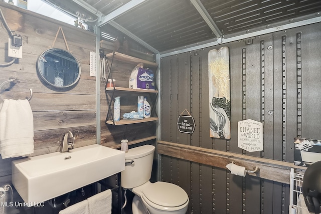 bathroom featuring toilet, lofted ceiling, wooden walls, and sink