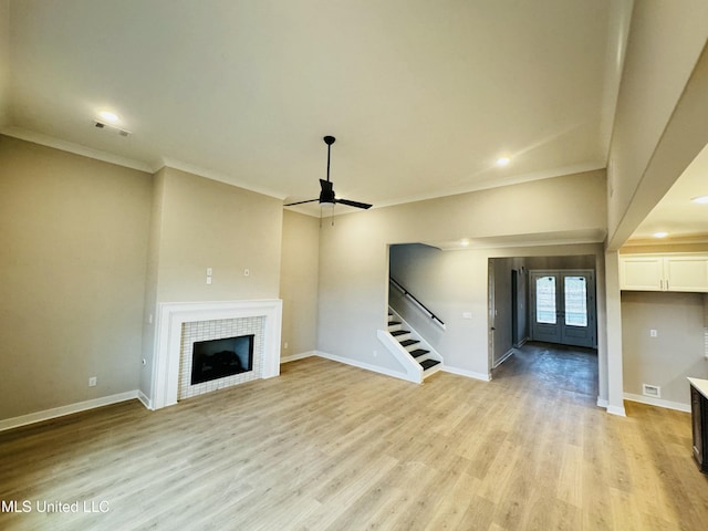 unfurnished living room with a tiled fireplace, ornamental molding, ceiling fan, light wood-type flooring, and french doors