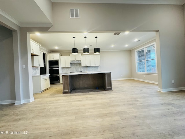 kitchen with pendant lighting, white cabinets, backsplash, a kitchen island with sink, and light hardwood / wood-style floors