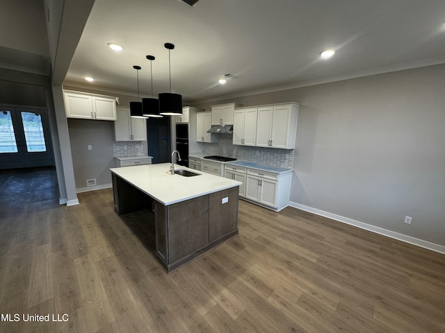 kitchen with decorative light fixtures, white cabinetry, sink, backsplash, and a center island with sink