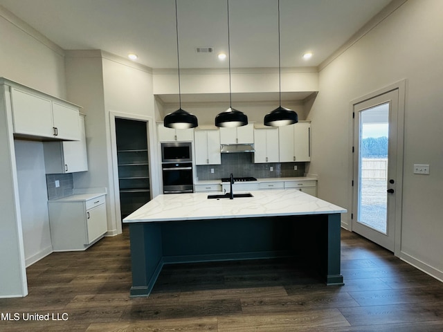 kitchen featuring appliances with stainless steel finishes, white cabinetry, hanging light fixtures, light stone counters, and a center island with sink