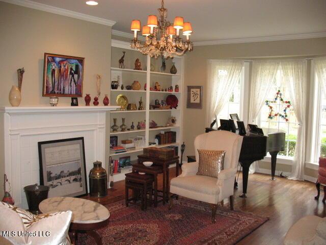 living area featuring a tile fireplace, crown molding, wood-type flooring, and a notable chandelier