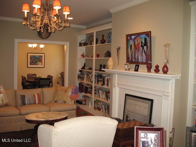 living room featuring a tile fireplace, ornamental molding, and a notable chandelier