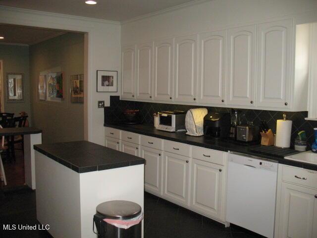 kitchen featuring backsplash, white dishwasher, crown molding, white cabinets, and a kitchen island