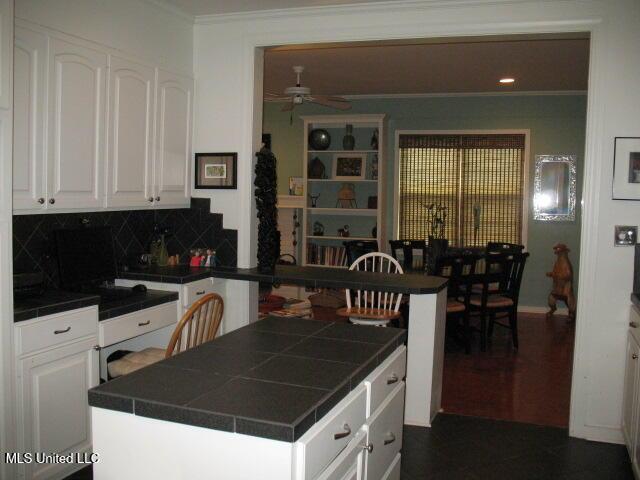 kitchen with white cabinets, a kitchen island, ceiling fan, and tile counters