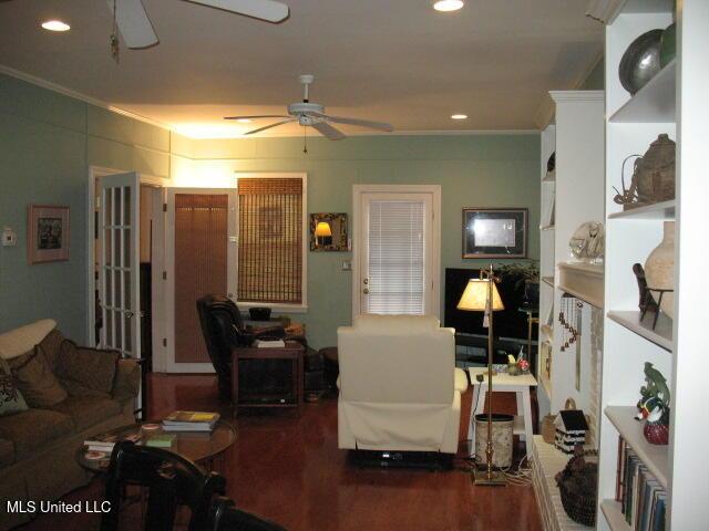 living room featuring dark hardwood / wood-style flooring, ceiling fan, and crown molding