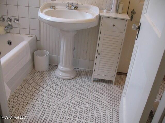 bathroom with tile patterned flooring, a washtub, sink, and tile walls