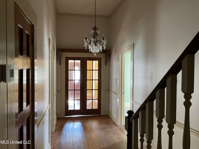 entryway with french doors, hardwood / wood-style flooring, ornamental molding, a towering ceiling, and a chandelier