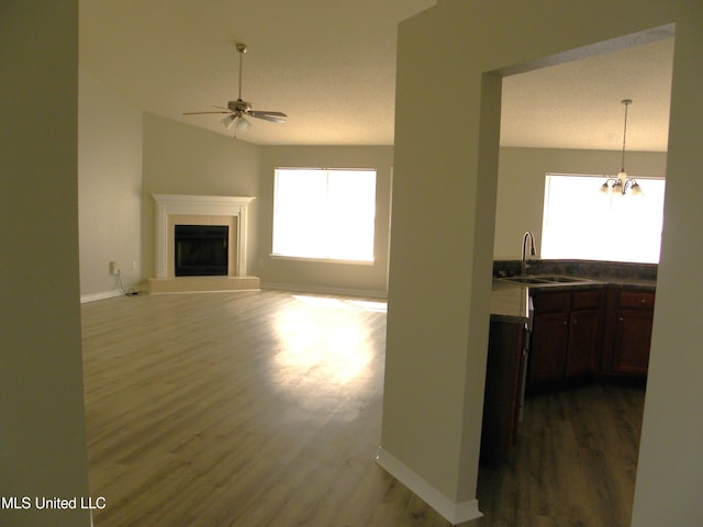 unfurnished living room with ceiling fan with notable chandelier, a tiled fireplace, sink, and dark hardwood / wood-style floors