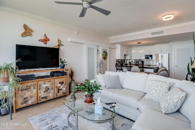 living room with light tile patterned floors, a ceiling fan, visible vents, and a textured ceiling