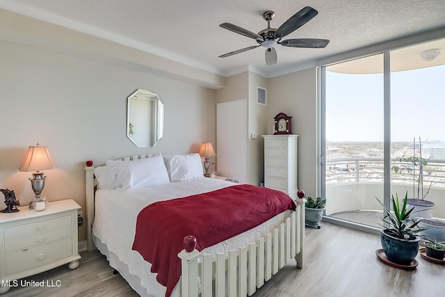 bedroom featuring light wood-type flooring, floor to ceiling windows, visible vents, and a textured ceiling