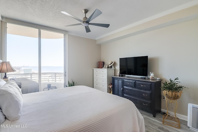 bedroom featuring baseboards, ceiling fan, a textured ceiling, light wood-style floors, and floor to ceiling windows