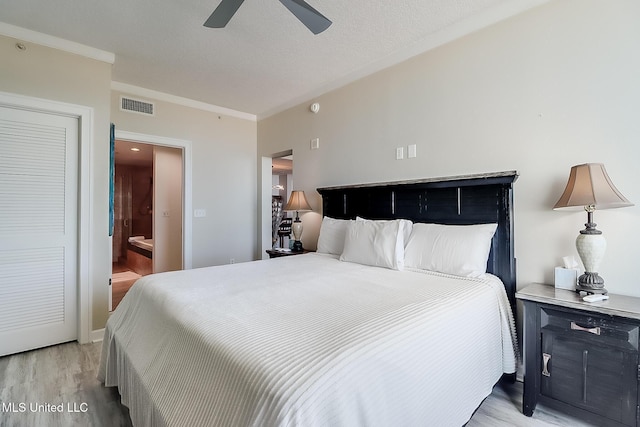 bedroom featuring ornamental molding, light wood-style flooring, a textured ceiling, and visible vents