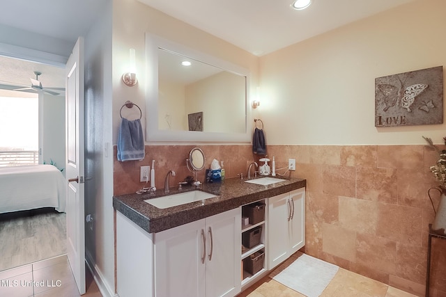 ensuite bathroom featuring connected bathroom, a sink, tile walls, and double vanity