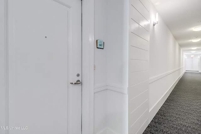 hall featuring dark colored carpet and baseboards