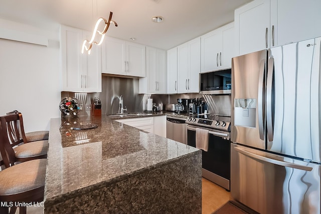 kitchen with stainless steel appliances, white cabinetry, a sink, dark stone counters, and a peninsula