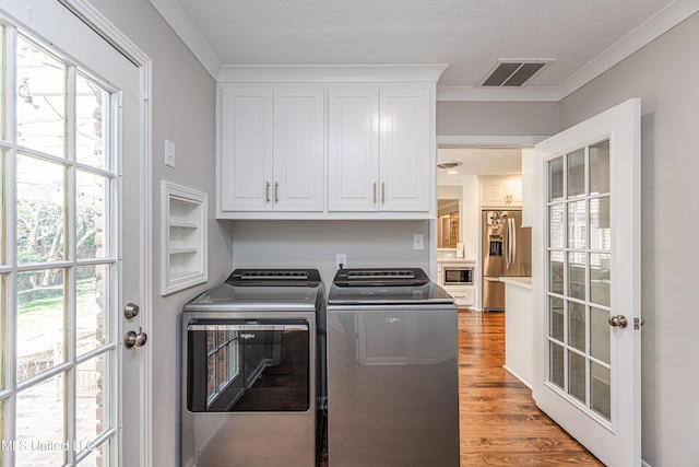 clothes washing area featuring ornamental molding, cabinet space, washing machine and clothes dryer, and wood finished floors