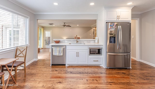 kitchen with stainless steel appliances, wood finished floors, a sink, and white cabinetry