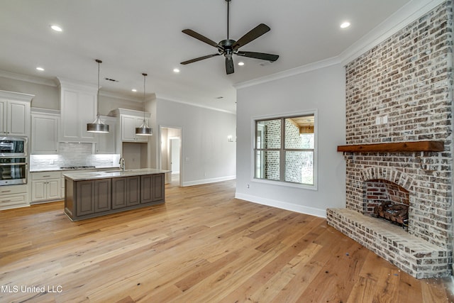 kitchen with white cabinetry, stainless steel appliances, pendant lighting, light hardwood / wood-style floors, and a center island with sink