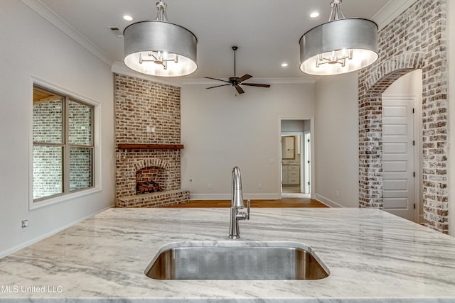 kitchen with pendant lighting, a fireplace, light stone counters, and sink