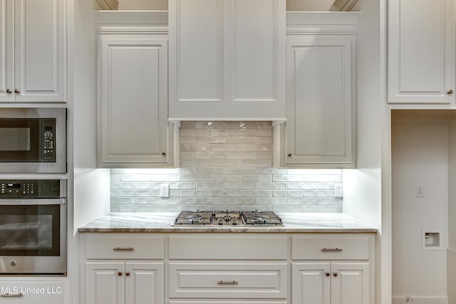 kitchen featuring decorative backsplash, appliances with stainless steel finishes, white cabinetry, and light stone counters