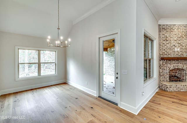 entryway featuring a brick fireplace, an inviting chandelier, light wood-type flooring, vaulted ceiling, and ornamental molding