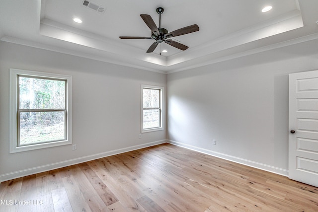 empty room with light wood-type flooring, ornamental molding, and a tray ceiling