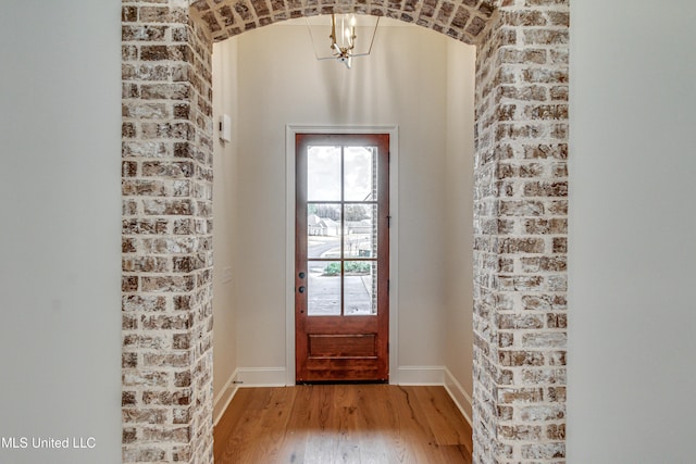 doorway to outside with hardwood / wood-style flooring, a notable chandelier, and brick wall