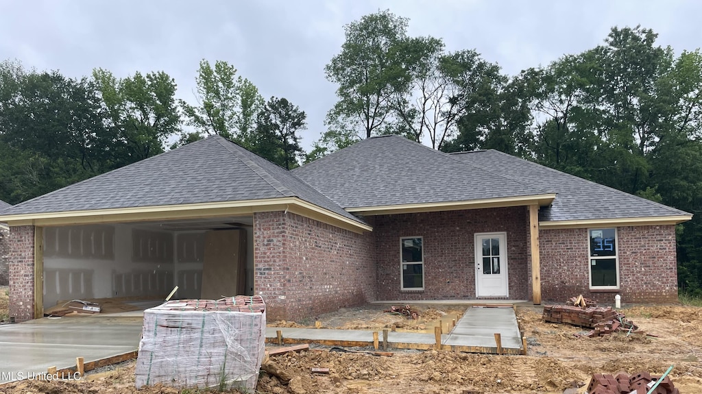 rear view of house featuring roof with shingles, brick siding, concrete driveway, and an attached garage