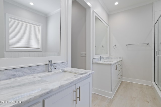 full bath with wood finished floors, two vanities, a stall shower, a sink, and crown molding