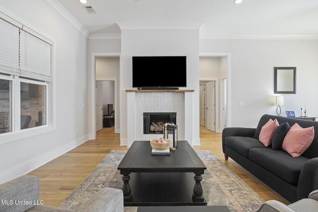 living room featuring visible vents, light wood-style flooring, a tile fireplace, and ornamental molding