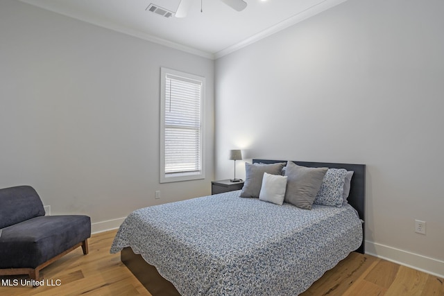 bedroom with visible vents, wood finished floors, baseboards, and ornamental molding