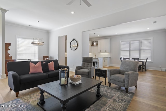 living area with baseboards, visible vents, light wood finished floors, ornamental molding, and ceiling fan with notable chandelier