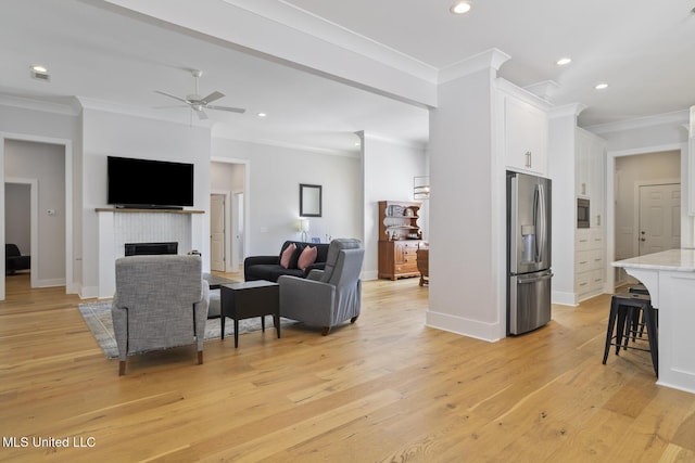 living area featuring crown molding, ceiling fan, recessed lighting, a fireplace, and light wood-style floors