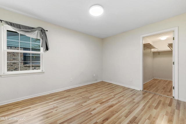 unfurnished bedroom featuring a spacious closet, a closet, and light hardwood / wood-style floors