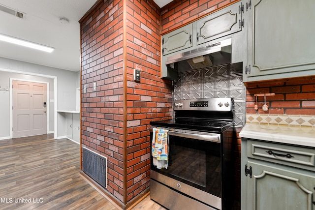 kitchen with dark hardwood / wood-style flooring, backsplash, stainless steel range with electric stovetop, and brick wall