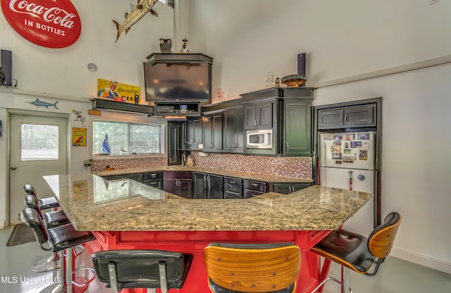 kitchen with a kitchen breakfast bar, stainless steel microwave, white refrigerator, and backsplash