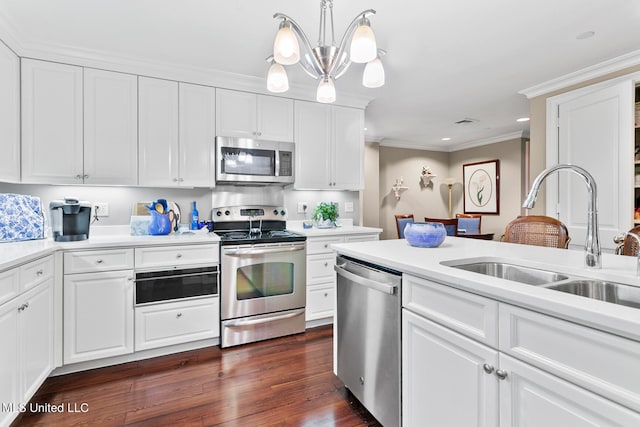 kitchen featuring appliances with stainless steel finishes, white cabinetry, pendant lighting, dark wood-type flooring, and crown molding