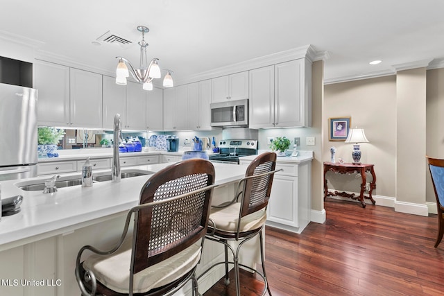 kitchen with white cabinets, hanging light fixtures, ornamental molding, dark hardwood / wood-style floors, and stainless steel appliances