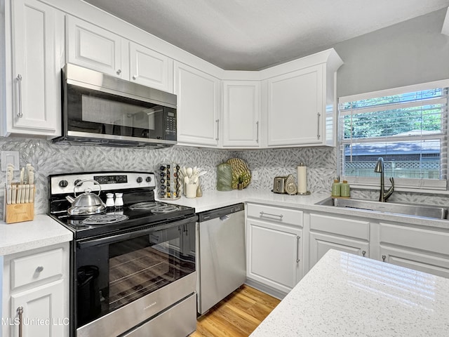 kitchen featuring appliances with stainless steel finishes, light wood-type flooring, decorative backsplash, sink, and white cabinetry