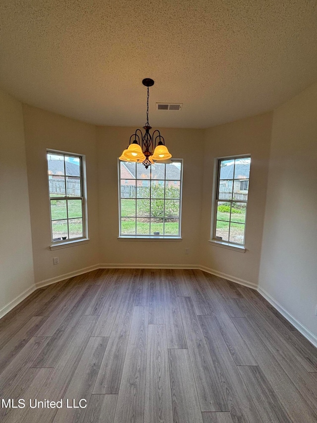 unfurnished dining area with an inviting chandelier, a textured ceiling, light wood-type flooring, and plenty of natural light