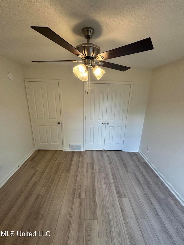 unfurnished bedroom featuring a closet, a textured ceiling, light hardwood / wood-style floors, and ceiling fan