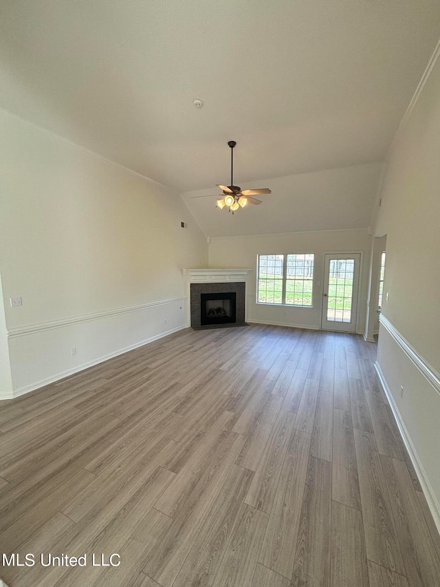 unfurnished living room featuring hardwood / wood-style floors, ceiling fan, a tiled fireplace, and vaulted ceiling