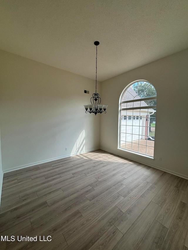 unfurnished dining area featuring hardwood / wood-style floors, a chandelier, and a textured ceiling