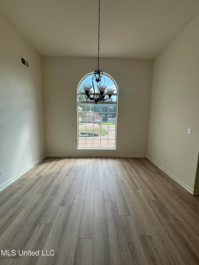 unfurnished dining area with an inviting chandelier, light hardwood / wood-style flooring, and a textured ceiling