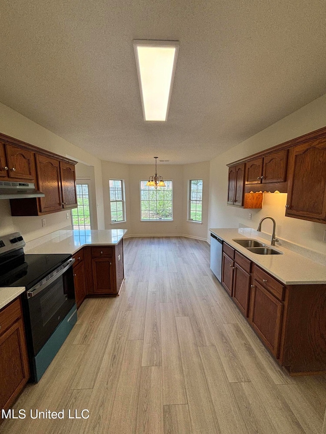 kitchen with kitchen peninsula, stainless steel appliances, sink, light hardwood / wood-style floors, and decorative light fixtures