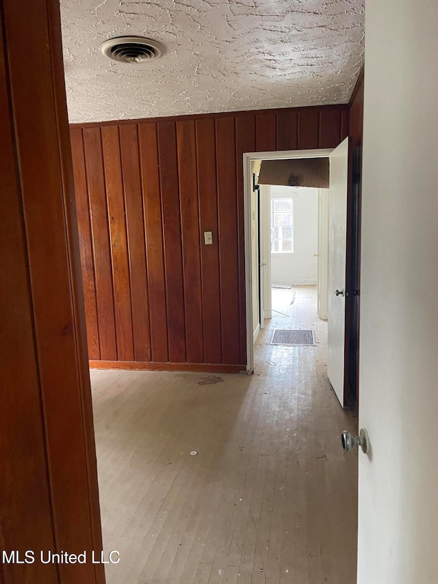 corridor featuring wood walls, light hardwood / wood-style floors, and a textured ceiling