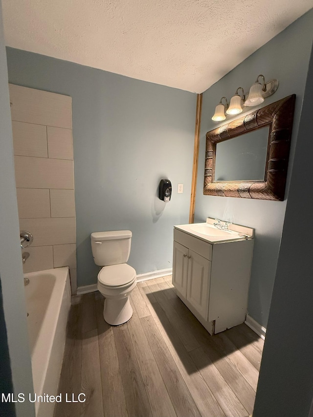 bathroom with toilet, wood finished floors, a tub to relax in, and a textured ceiling